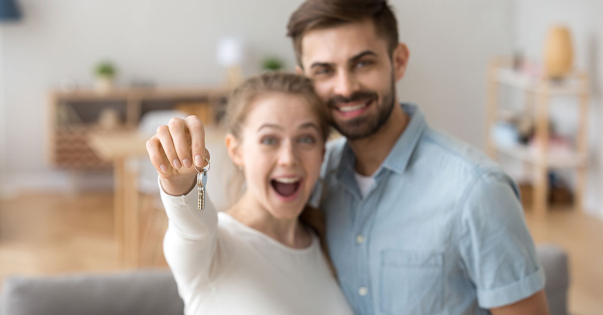 First-time home buying couple holds up the keys to their new home