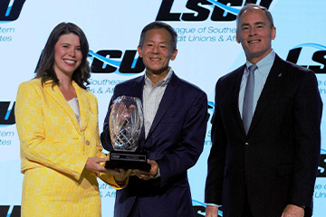 John Hirabayashi accepting the LSCU award on stage, smiling as he holds the trophy.