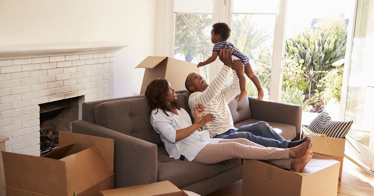 Proud new homeowners take a break from unpacking and play with their baby on the couch.