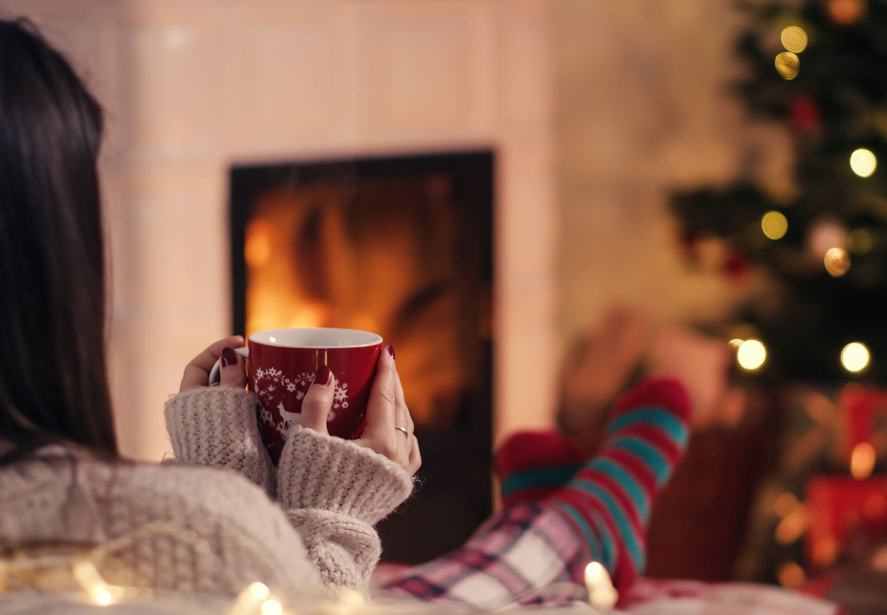 a woman relaxing in front a fire and holiday tree.