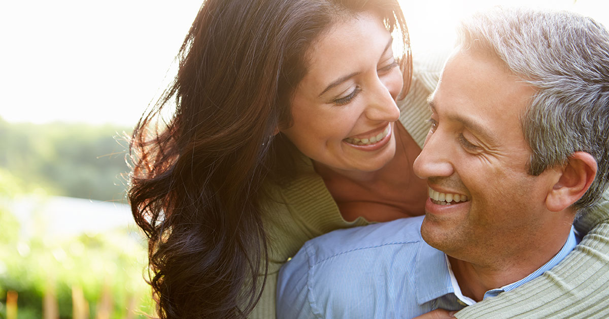 A smiling couple in their 40s with the woman leaning her head over his shoulder.