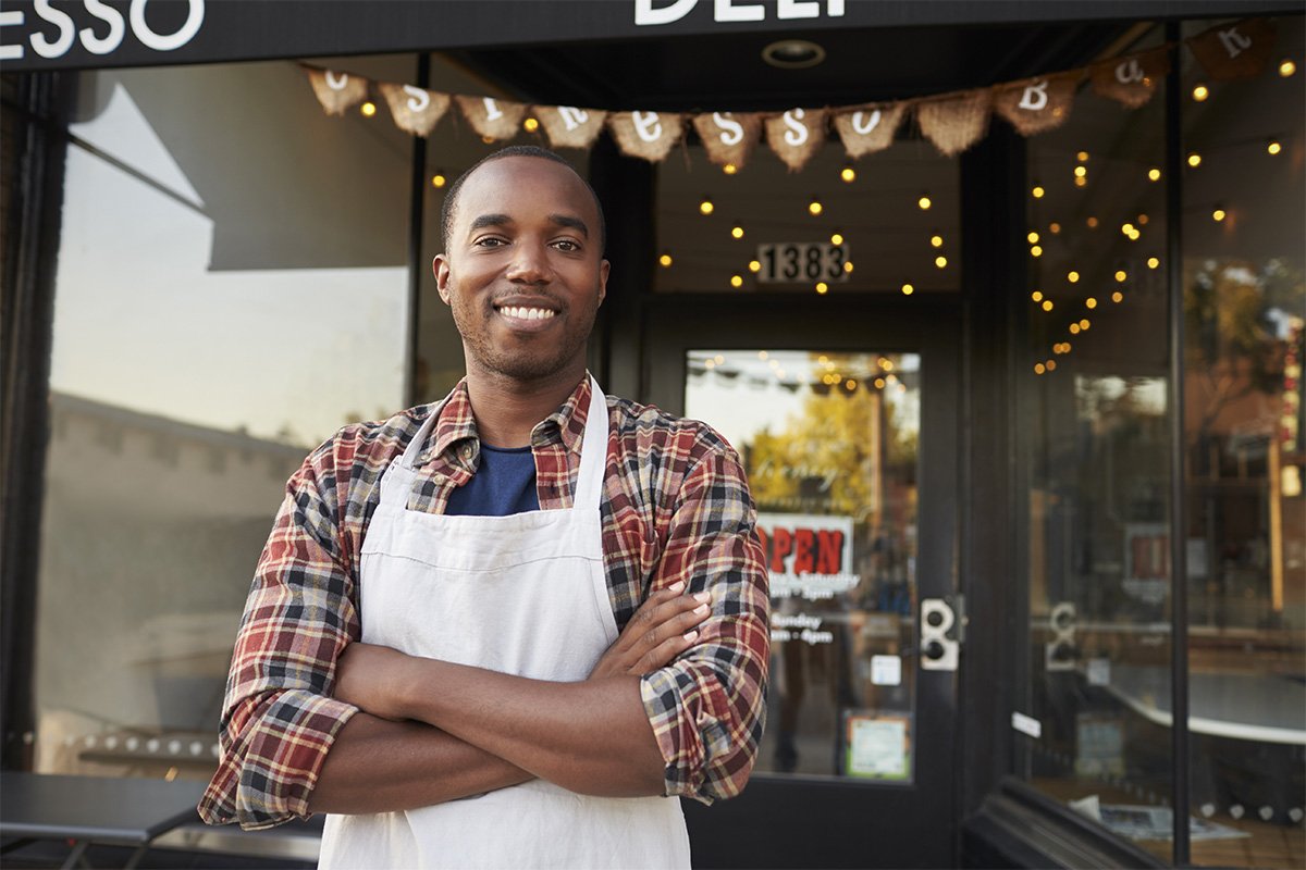 Business owner with an apron on and arms crossed posing outside a store.