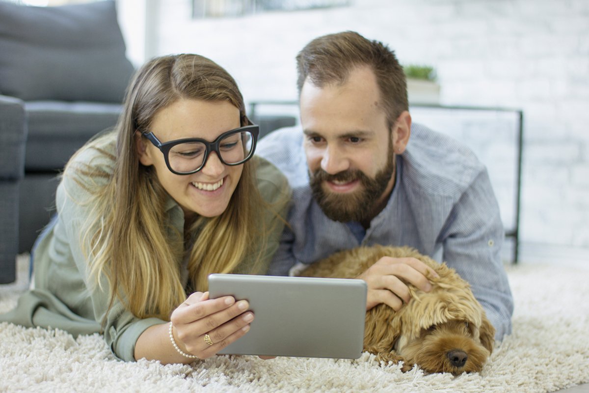 couple with a dog on the carpet looking at a tablet