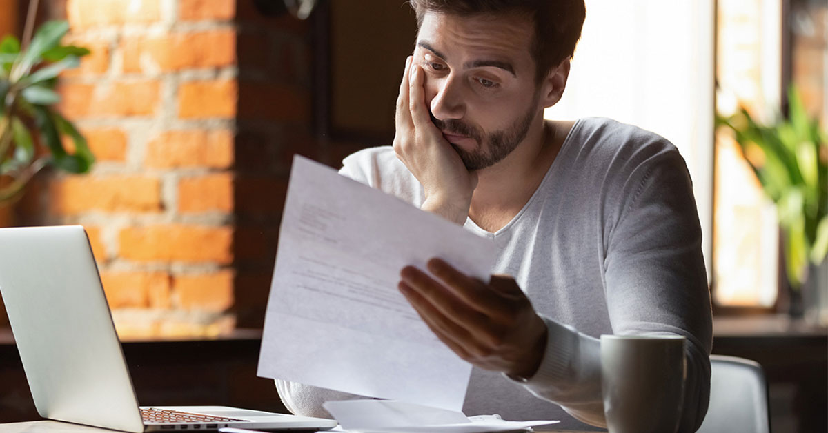 Man seated in front of a laptop at his apartment, examining a new medical bill.