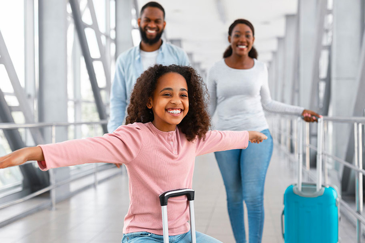 Parents and daughter walking with luggage smiling.