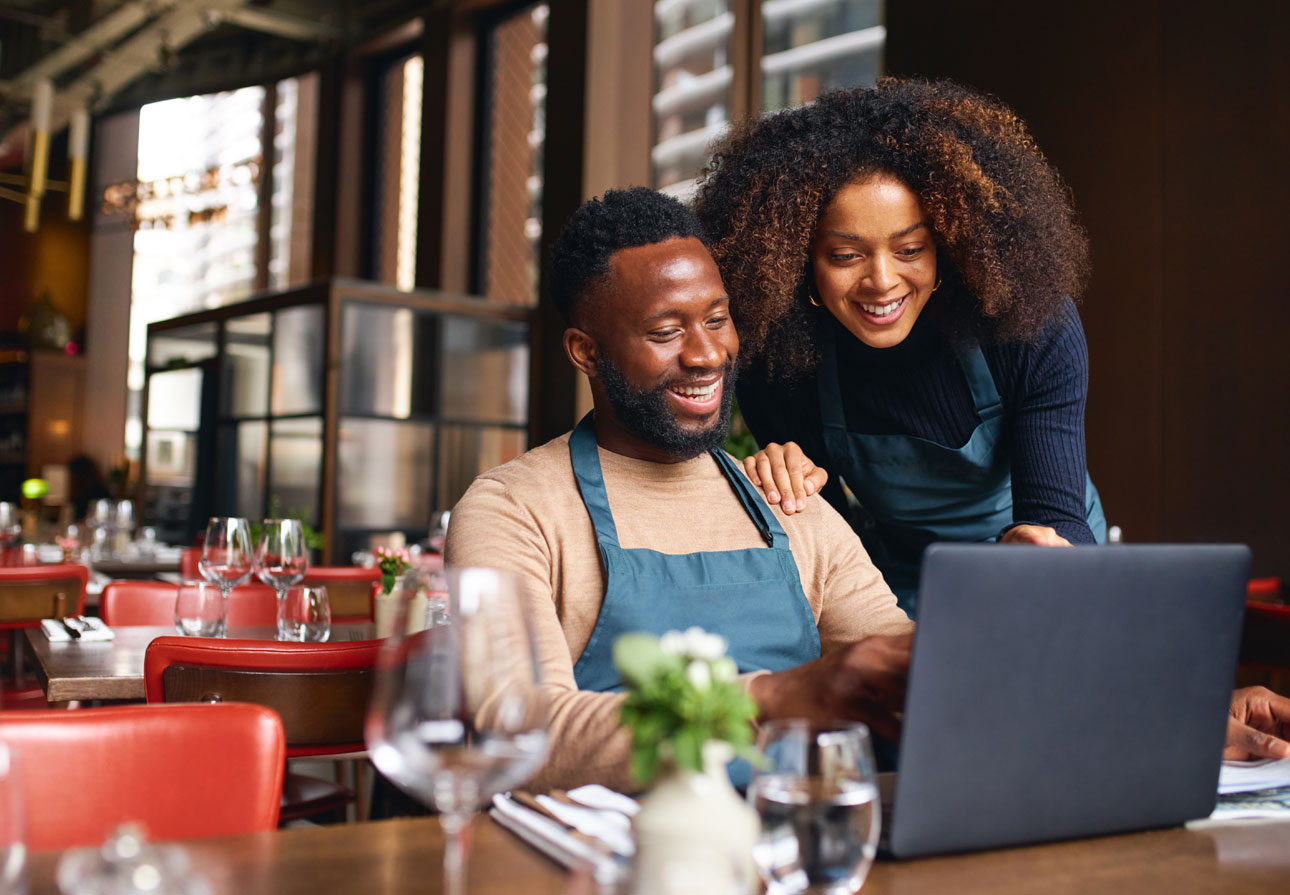 two business owners looking at their laptop in their restaurant.