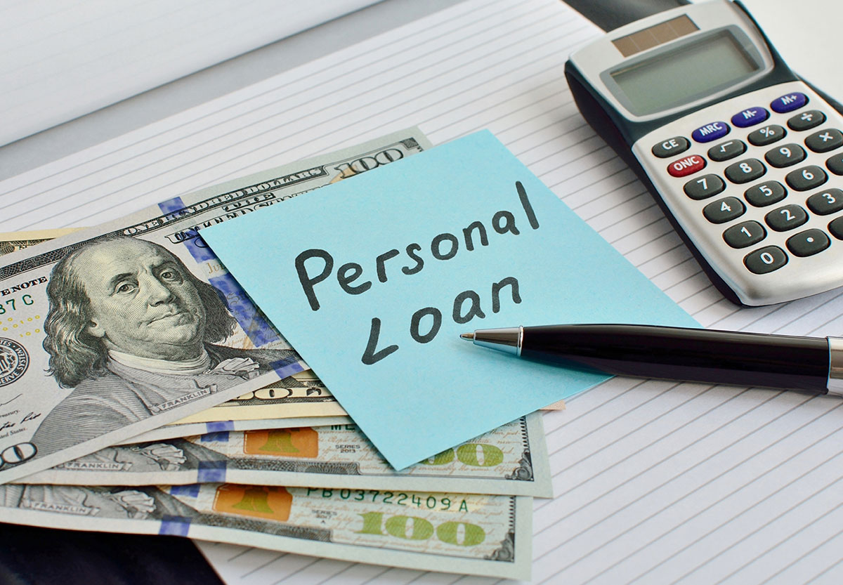 a notepad with money, a note that says, ‘personal loan,’ a pen, and a calculator on top of it.