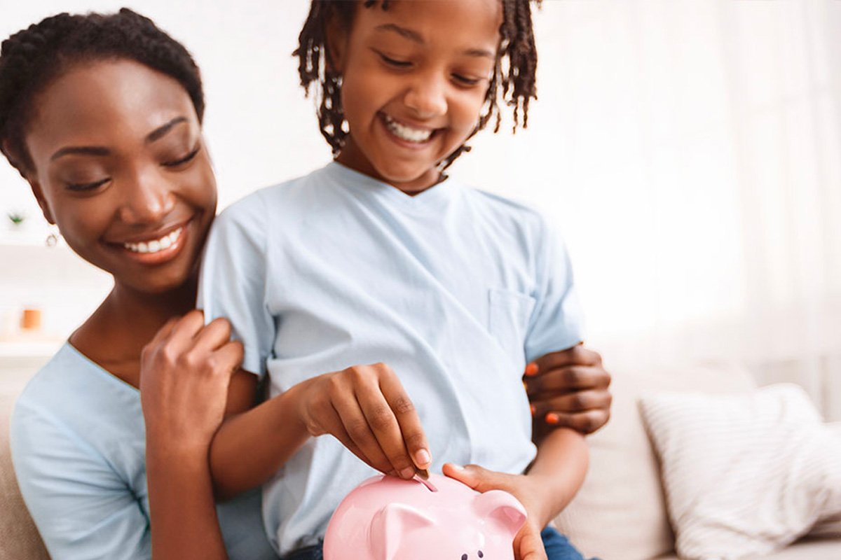 Mother and daughter placing coins into a piggy bank.