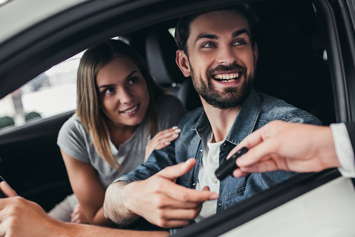 A smiling couple sitting inside their new car, receiving the keys.