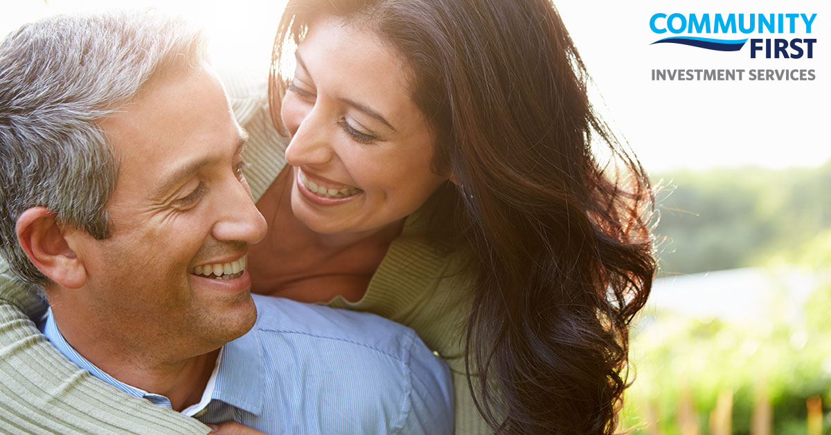 A smiling couple in their 40s with the woman leaning her head over his shoulder.
