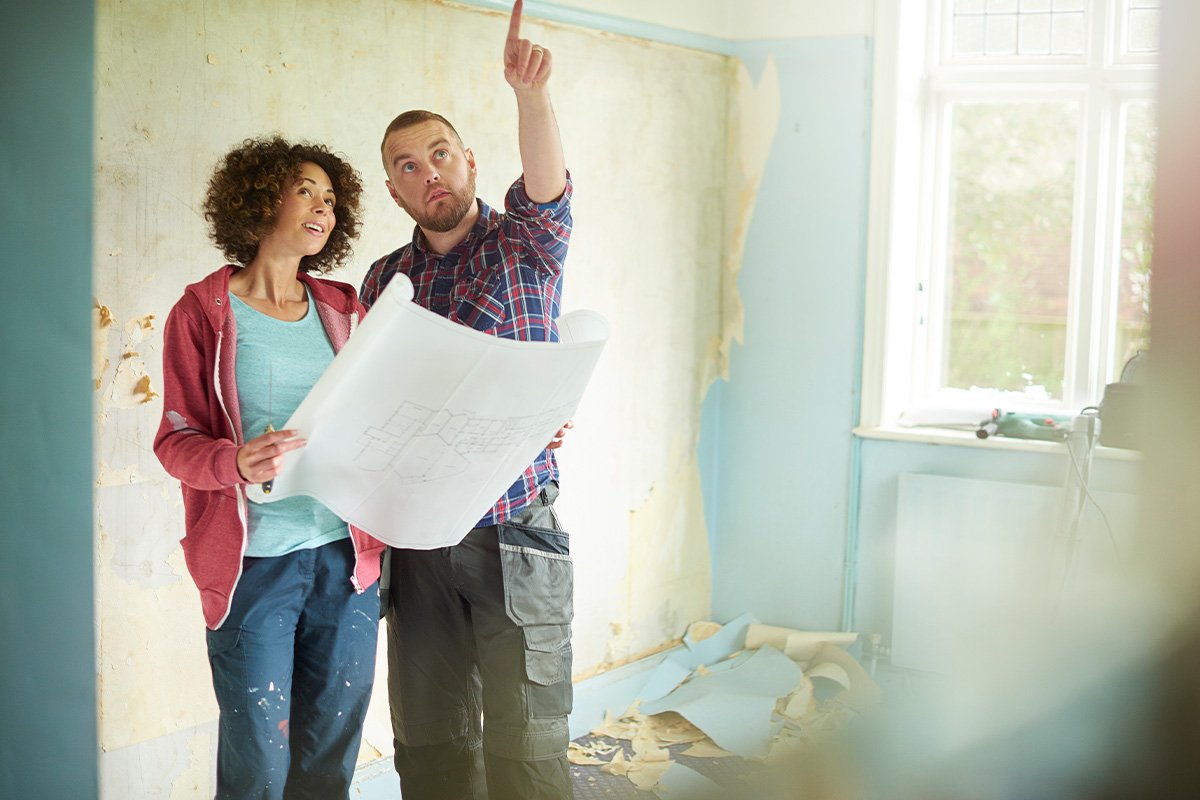couple holding home improvement plans while looking up