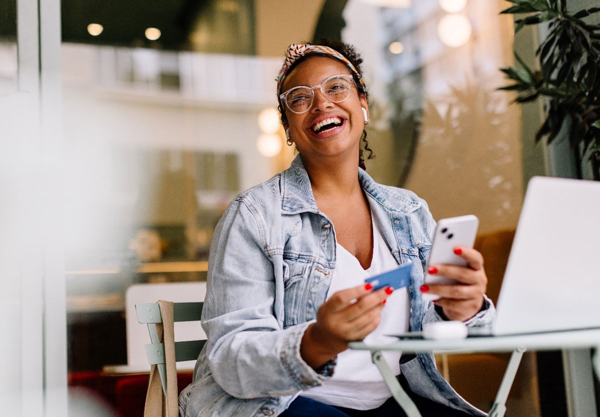 Woman sitting in a café and using her smartphone for online shopping, paying with a credit card.