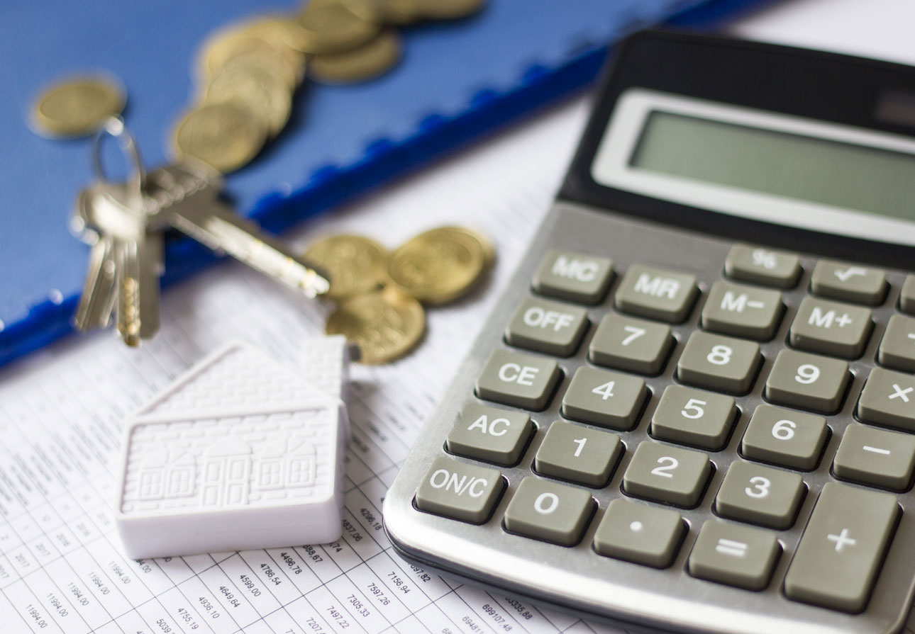 a calculator sitting next to a miniature home, keys, and coins.