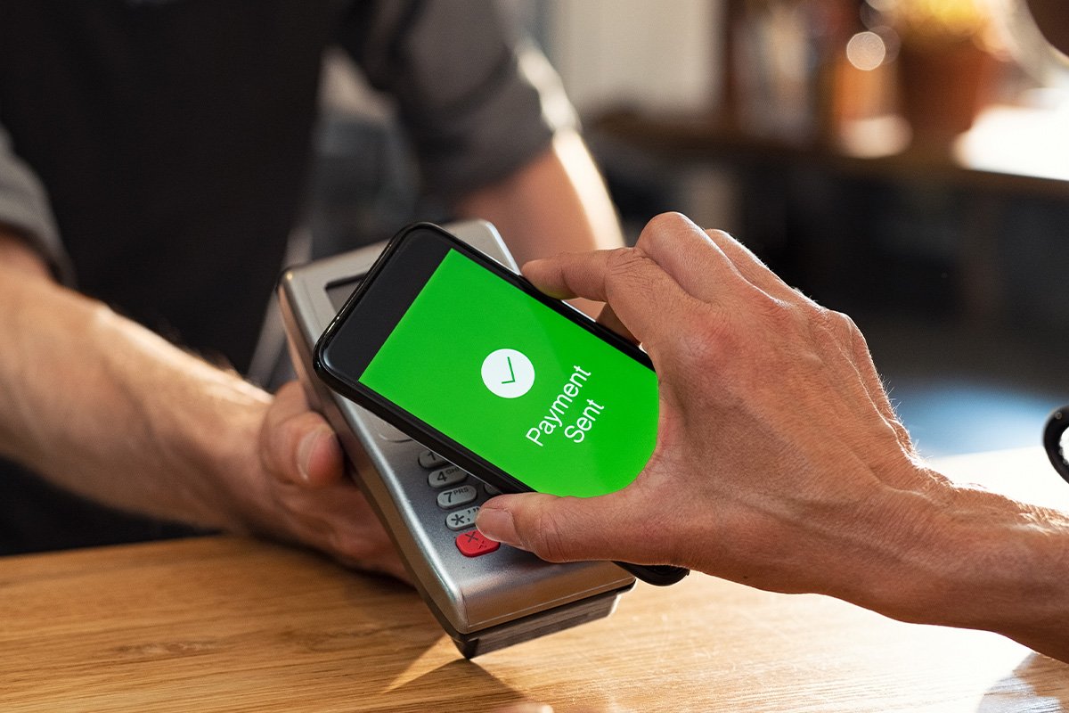 A person paying with his cell phone. On his cell phone there is a green screen with an approved symbol.