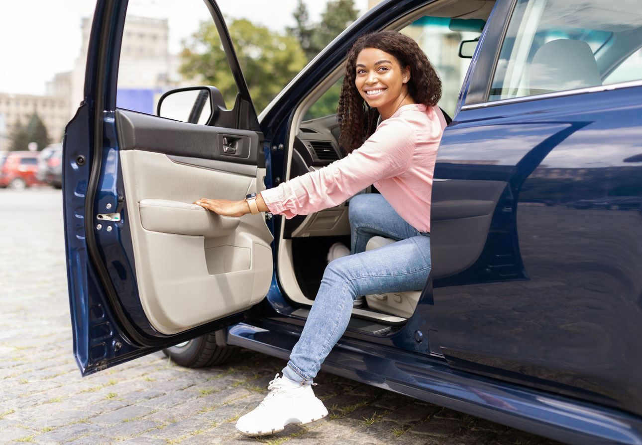 a smiling, young woman stepping into her vehicle.