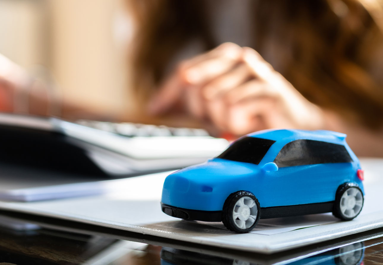 a small toy car sitting on a desk next to a woman using a calculator.