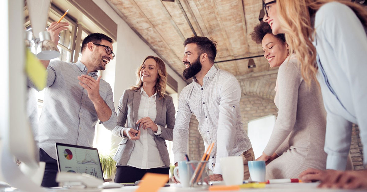 Team of young professionals smiles as they discuss business around a conference table.