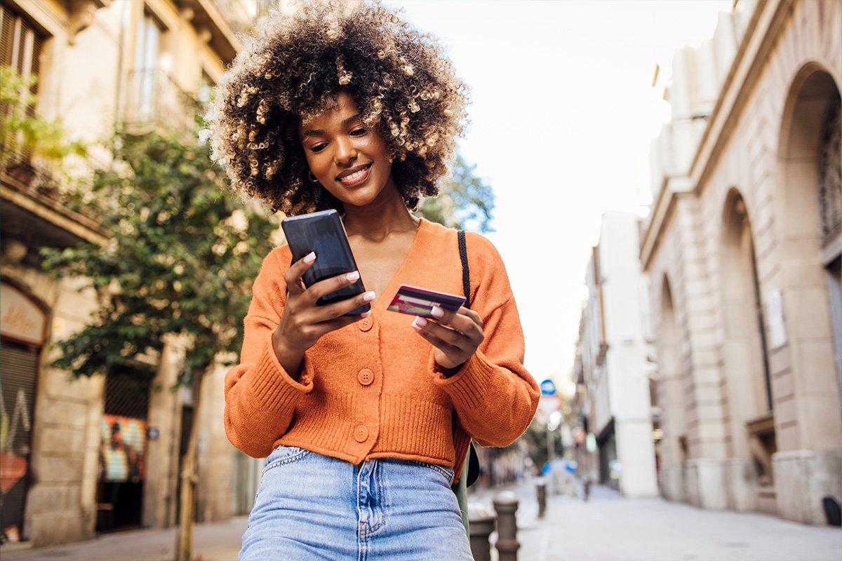 woman smiling while holding a cell phone and a credit card