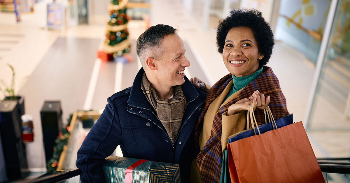 Happy couple smiles as they hold their holiday shopping bags on an escalator at the mall.